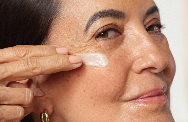 Foto en primer plano del perfil lateral de una persona con piel clara, aplicando producto para las arrugas.